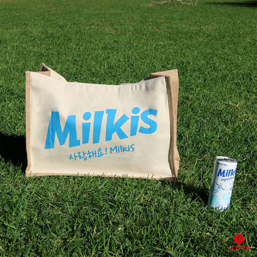 Milkis beige tote bag with blue logo outdoors on grass, shown with a Milkis original drink can