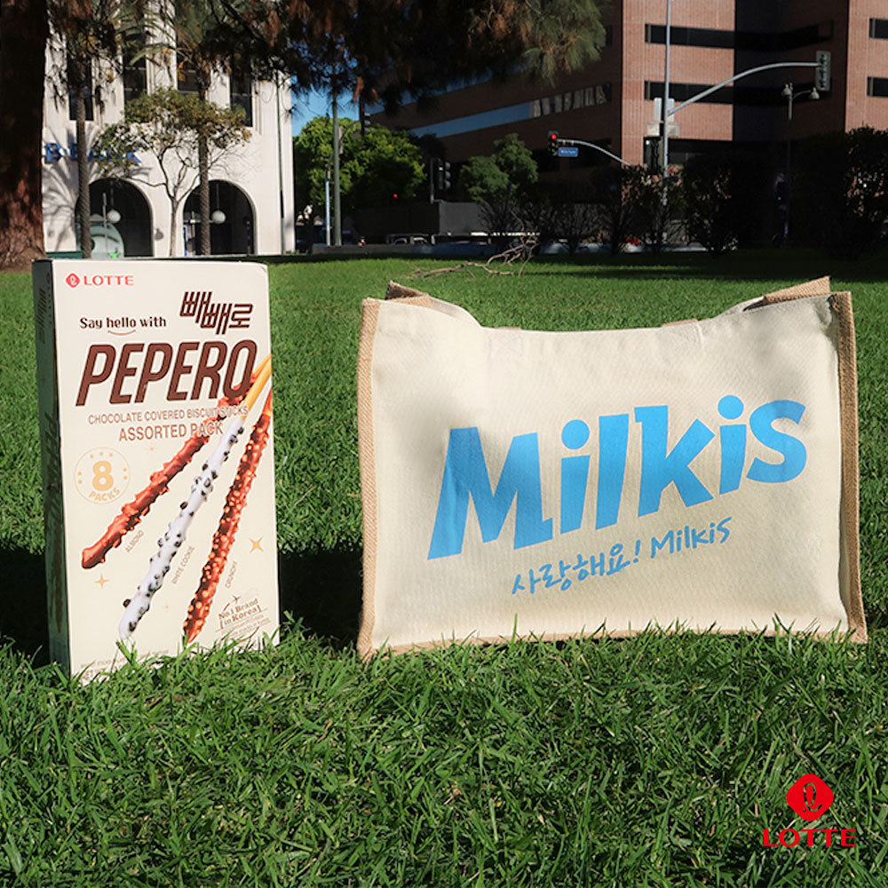 Milkis beige tote bag with blue logo displayed outdoors on grass next to a Lotte Pepero assorted box
