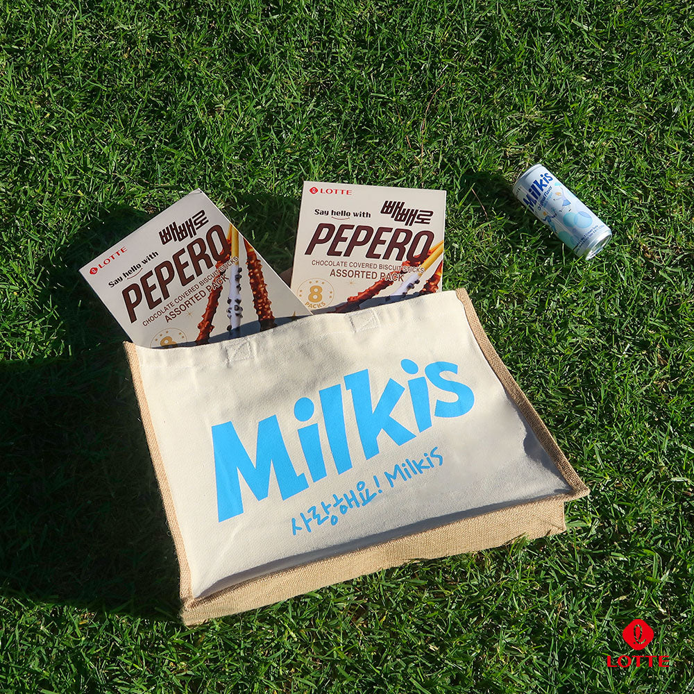 Milkis beige tote bag with blue logo filled with Lotte Pepero boxes, shown outdoors on grass with a Milkis drink can