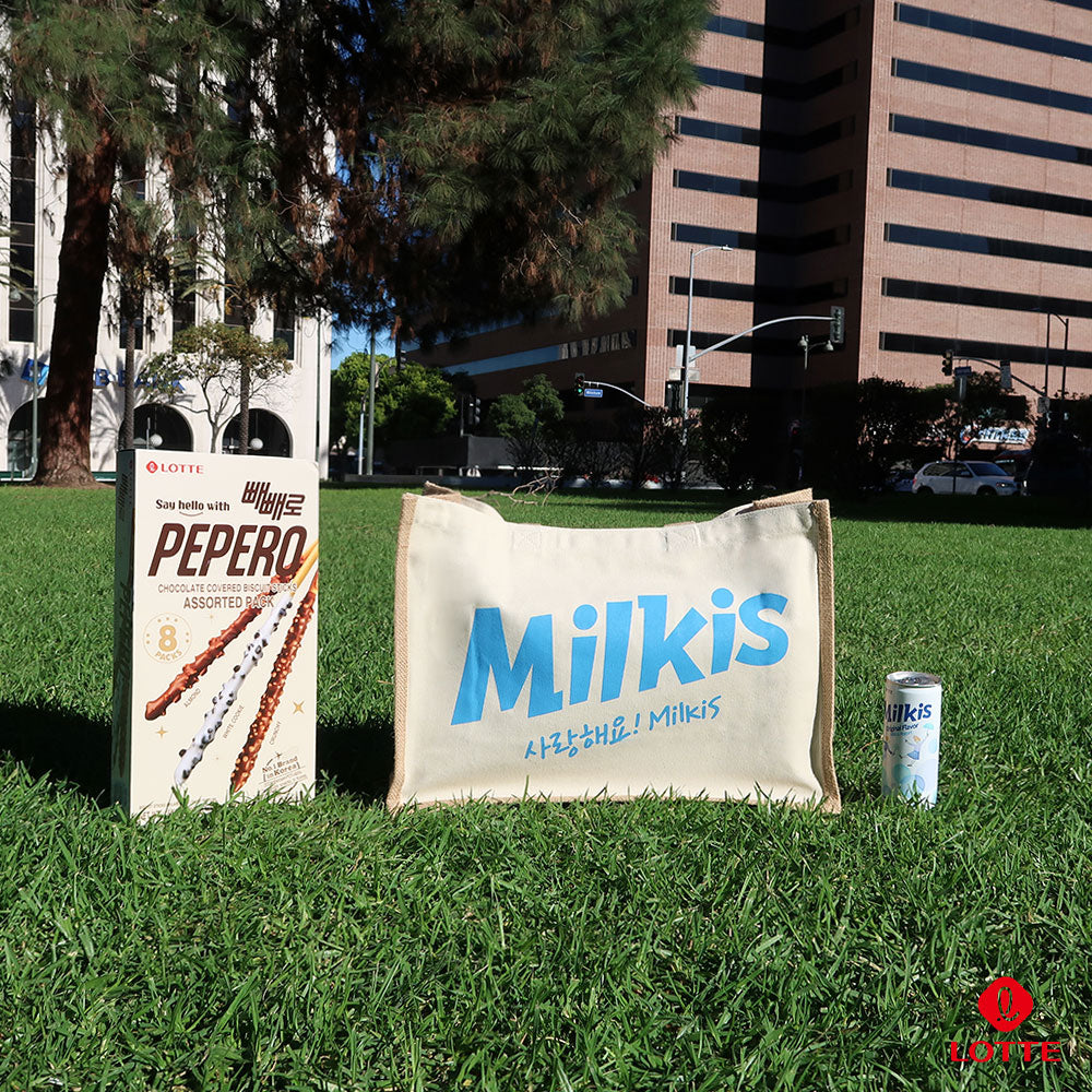 Milkis beige tote bag with blue logo, Pepero pack, and Milkis soda on green grass.